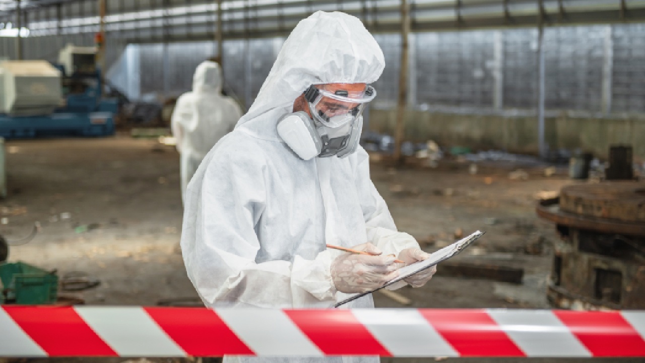 Worker wearing protective coveralls and a respirator inspecting a potentially hazardous industrial site.